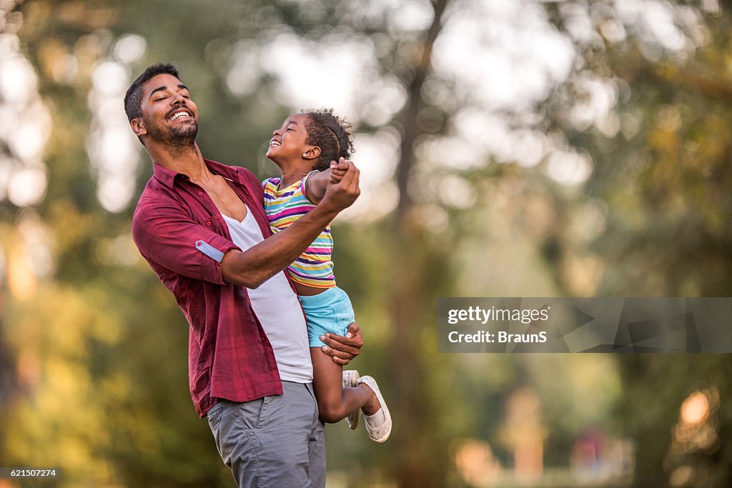 Happy African American father dancing with his cute daughter outdoors.