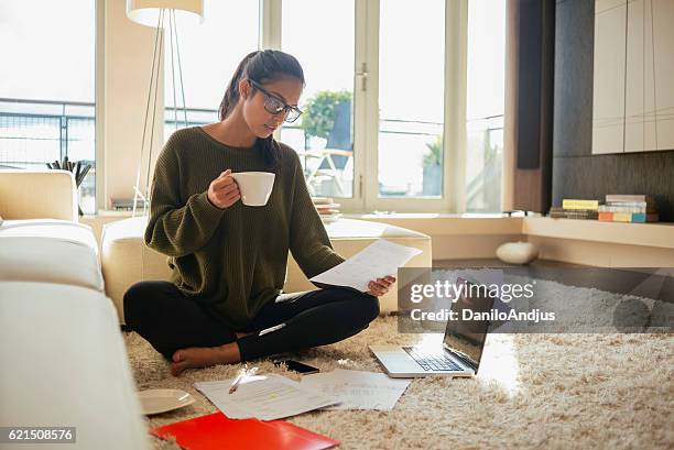 young woman reading paperwork in her living room, - heat pad stock pictures, royalty-free photos & images