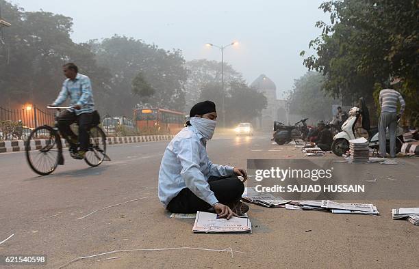 An Indian newspaper vendor wears a mask whilst he sorts news papers on a road as heavy smog covers New Delhi on November 7, 2016. Schools in the...