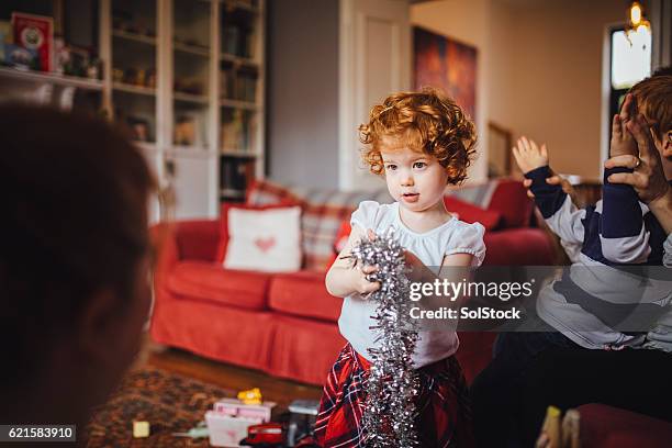 kleines mädchen hilft ihrer mutter mit den weihnachtsdekorationen - tinsel stock-fotos und bilder