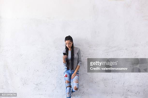young asian woman leaning back on blank wall - phone leaning stock pictures, royalty-free photos & images