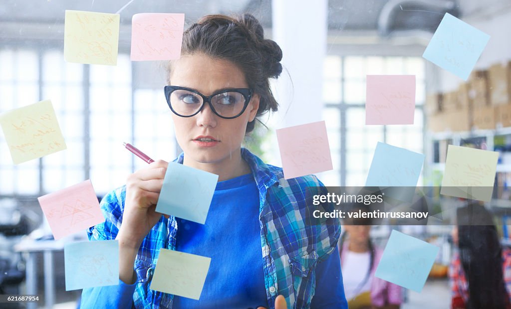 Young woman writing on post-it notes on glass wall