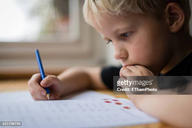 schoolboy at his desk doing his maths homework - kid thinking stock-fotos und bilder