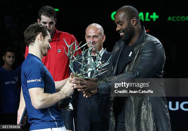 Winner Andy Murray of Great Britain receives the trophy from gold medalist in Rio Teddy Riner while Director of the tournament Guy Forget looks on...