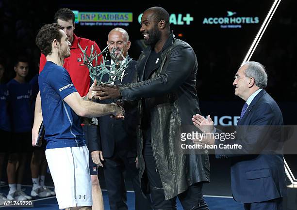 Winner Andy Murray of Great Britain receives the trophy from gold medalist in Rio Teddy Riner while Director of the tournament Guy Forget and...