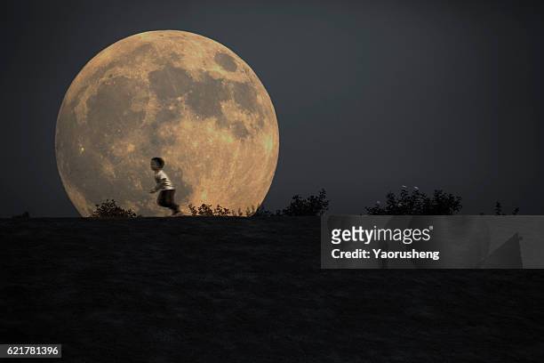 silhouette of a young boy running in front of the full moon - mini moon stock pictures, royalty-free photos & images