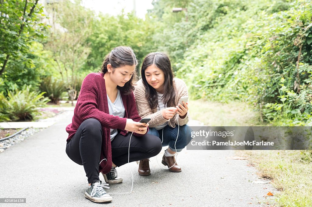 Teenaged Eurasian Sisters Jouant à des jeux de réalité augmentée sur smartphones