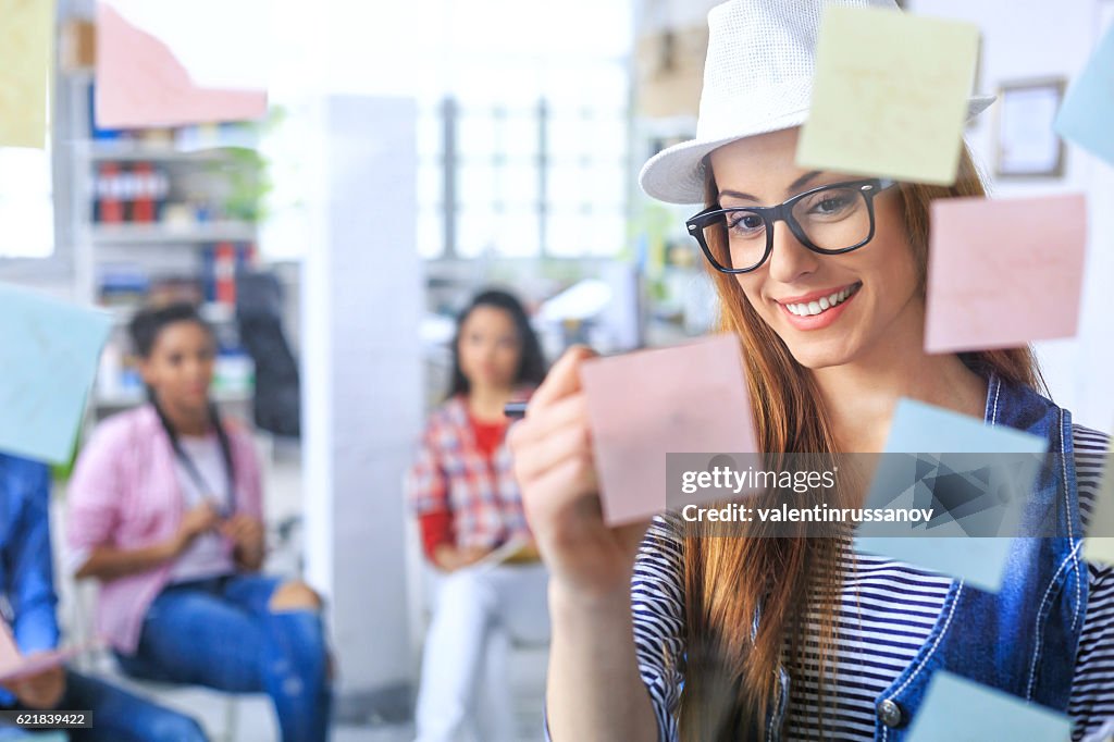 Donna sorridente con cappello e occhiali che scrivono su note post-it