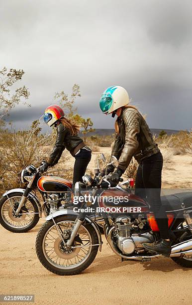 Two young women riding motorcycles on empty road