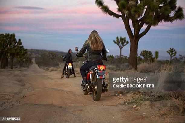 two young women riding motorcycles on empty road - brook steppe photos et images de collection