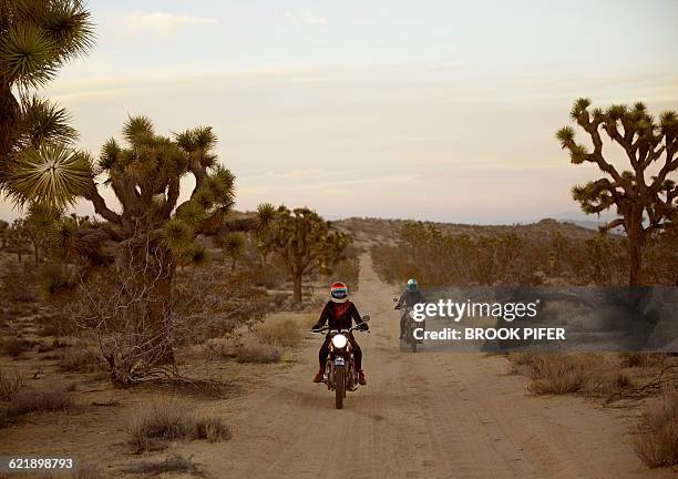 two young women riding motorcycles on empty road - dirt road motorbike stock pictures, royalty-free photos & images