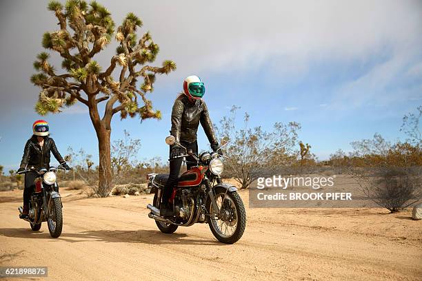 two young women riding motorcycles on empty road - motorbike ride stockfoto's en -beelden