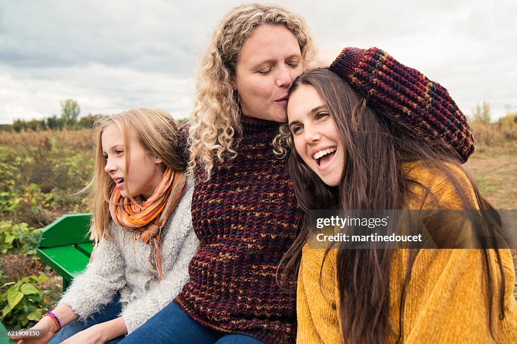 Mother kissing teenage daughter strolling in trailer in field.