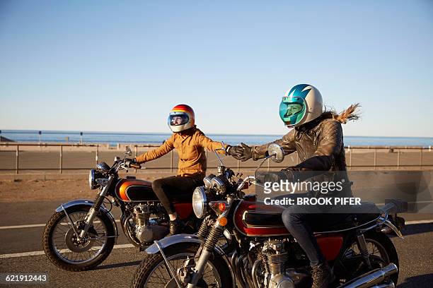 Two young women riding motorcycles on empty road