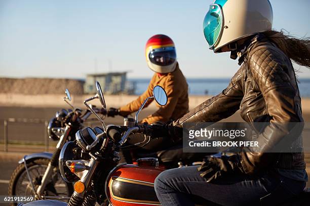 two young women riding motorcycles on empty road - mare moto foto e immagini stock