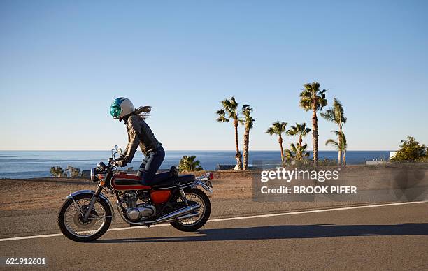 young woman riding motorcycle on empty road - autoroute stock-fotos und bilder