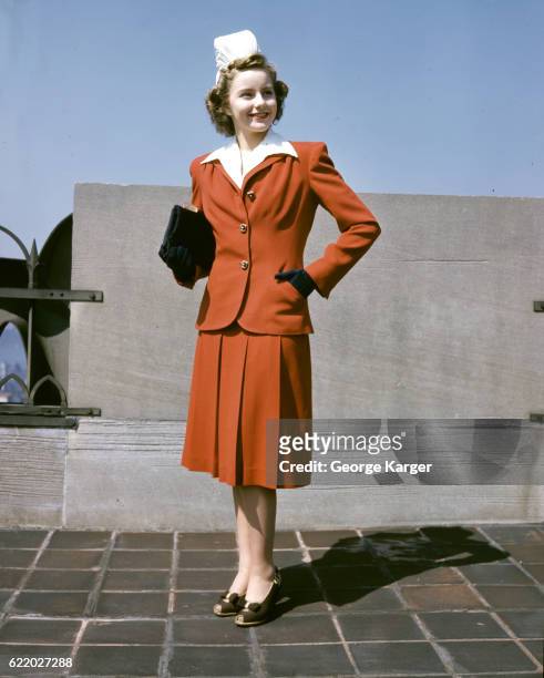 Woman modeling a red wool suit with coat and pleated skirt, 1941.
