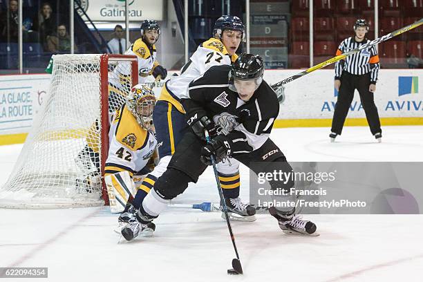 Vitalii Abramov of the Gatineau Olympiques controls the puck against Nicholas Welsh of the Shawinigan Cataractes as Mikhail Denisov guards his net on...