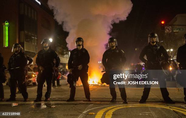 Police hold a skirmish line as a trash fire lit by protesters burns during an anti-Trump protest in Oakland, California on November 9, 2016....