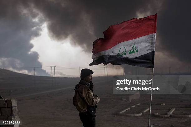 Fighter from a local tribe keeps watch from his rooftop outpost under smoke filled skies from burning oil wells set on fire by fleeing ISIS members...