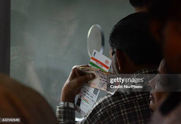 An indian man stands in a queue ,carring 1000 rupee notes and Aadhar card , as he waits his turn to exchange his currency with 100 rupee notes , in a...