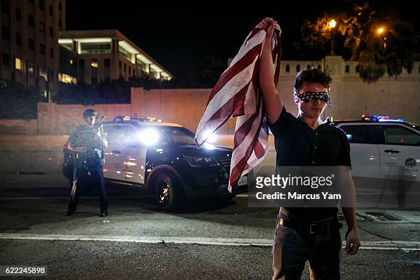 An anti-Trump protester stands in defiance blind folded and holding an American flag in front of police officers, as protesters block up the 101...