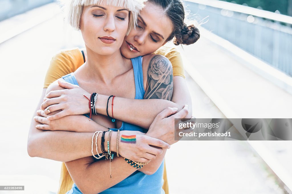 Two women embracing on bridge with eyes closed