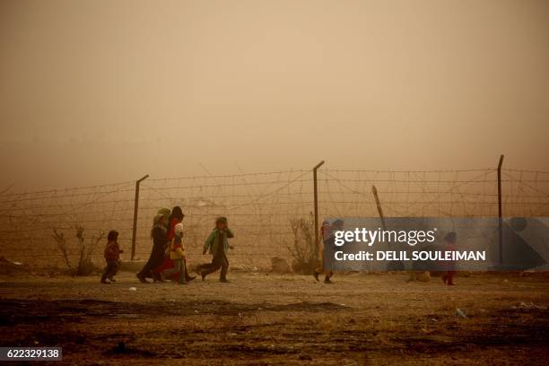 Syrian children walk around the camp grounds during a sandstorm at a temporary refugee camp in the village of Ain Issa, housing people who fled...