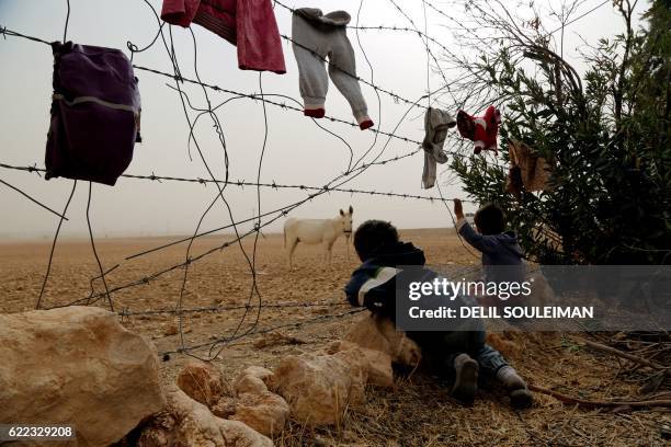 Syrian children look at a donkey from behind the fence at a temporary refugee camp in the village of Ain Issa, housing people who fled Islamic State...