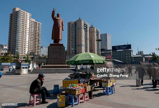 Vendor selling food and drinks under the statue of Mao Zedong on the square of Dandong railway station.