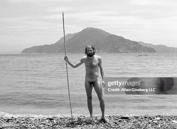 Beat poet Allen Ginsberg, wearing only his birthday suit, poses with a bamboo stick in his hand on the beach.