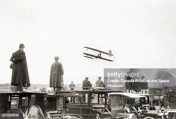 Spectators standing on cars watch Count Charles de Lambert fly a Wright Flyer in the 1909 Grande Quinzaine de Paris.