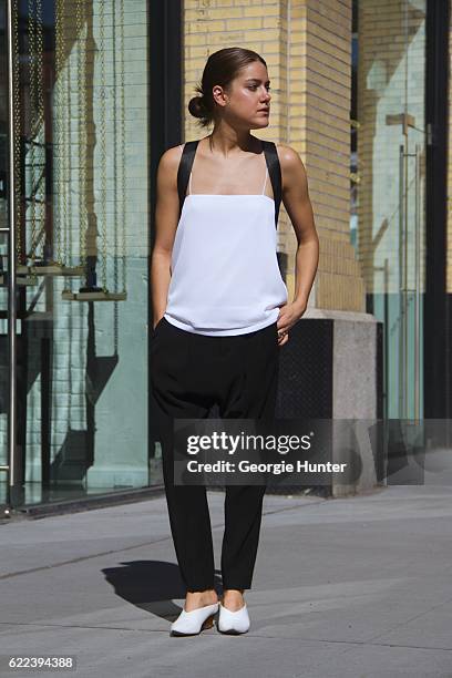 Emma Sousa wearing monochrome look of loose AYR white silk layered top with thin spaghetti straps, AYR tailored black suit pants, white leather Cline...