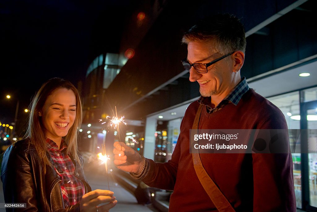 Smiling couple holding Christmas sparklers  at night outside