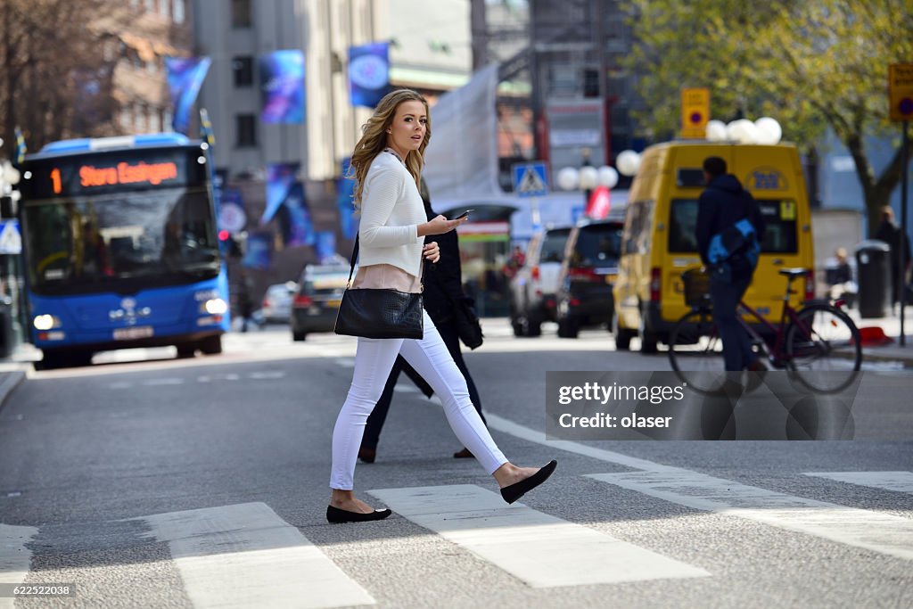 Mulher atravessando rua, travessia de zebra, ônibus e trânsito no fundo