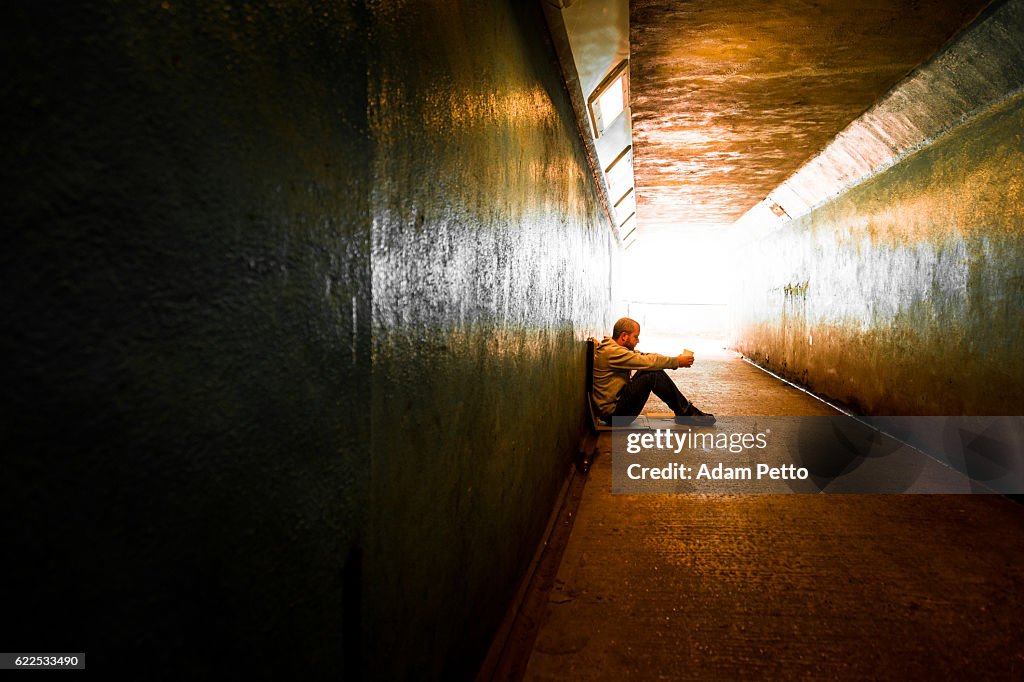 Young homeless adult male sitting and begging in subway tunnel