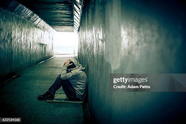 homeless adult male sitting in subway tunnel, hands on head - drug abuse stock pictures, royalty-free photos & images