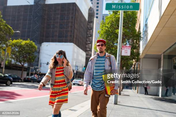 Couple walk together on the sidewalk along a city street, San Francisco, California, September 4, 2016. .