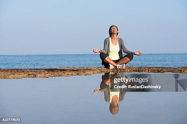 african woman meditating on seashore. - half lotus position stock pictures, royalty-free photos & images