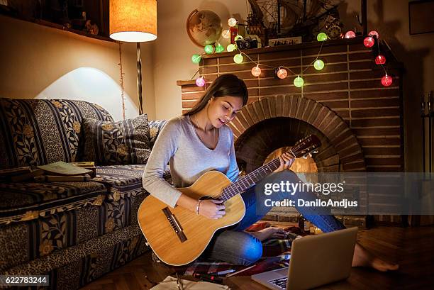 young woman playing the guitar next to the fireplace - hot latin nights stock pictures, royalty-free photos & images