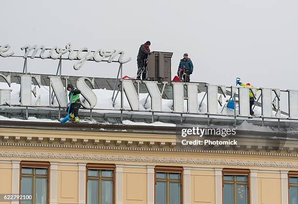 snow shoveling a roof in stockholm's old town - vinter stockfoto's en -beelden