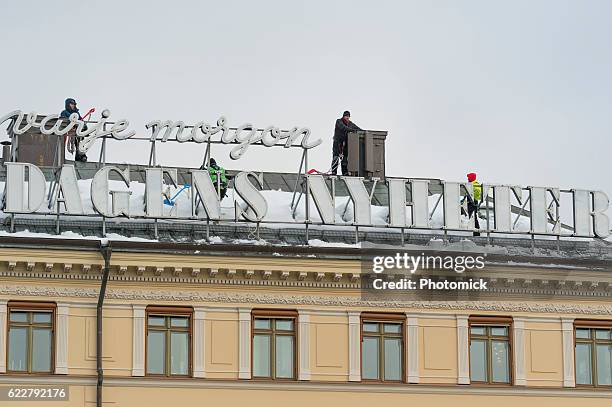 snow shoveling a roof in stockholm's old town - vinter stockfoto's en -beelden