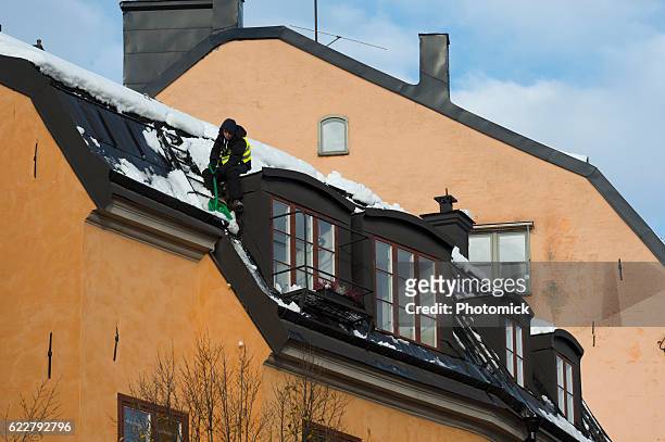 snow shoveling a roof in stockholm's old town - vinter stockfoto's en -beelden