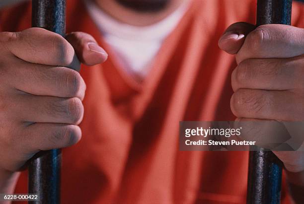 prisoner holding bars of cell - häftling stock-fotos und bilder