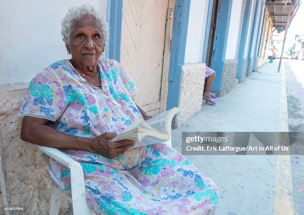 Panama, Province of Panama, Panama city, Old panamean woman reading in front of her house in the street in Casco Viejo...
