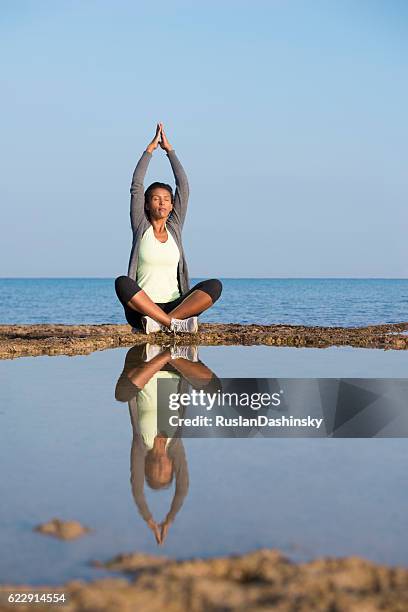 frau, die yoga in lotusposition am meer übt. - halber lotussitz stock-fotos und bilder