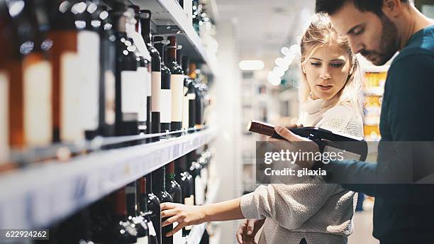 couple buying some wine at a supermarket. - wine shelf stock pictures, royalty-free photos & images