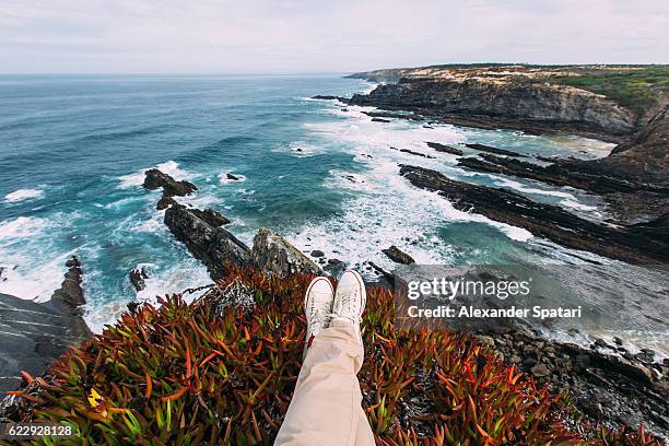 personal perspective of feet in white canvas shoes with the view towards ocean and cliffs, high angle view - alentejo photos et images de collection