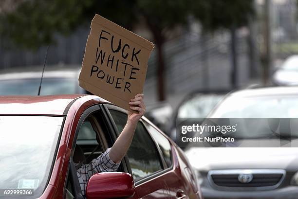 Motorist holds a sign while waiting for crowd of anti-Trump protesters to pass by in Los Angeles, California on November 12, 2016. According to the...