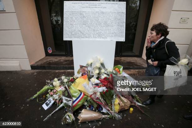 Woman gestures next to a commemorative plaque reading "In memory of the injured and killed victims of the attacks of November 13, 2015 - to the 90...